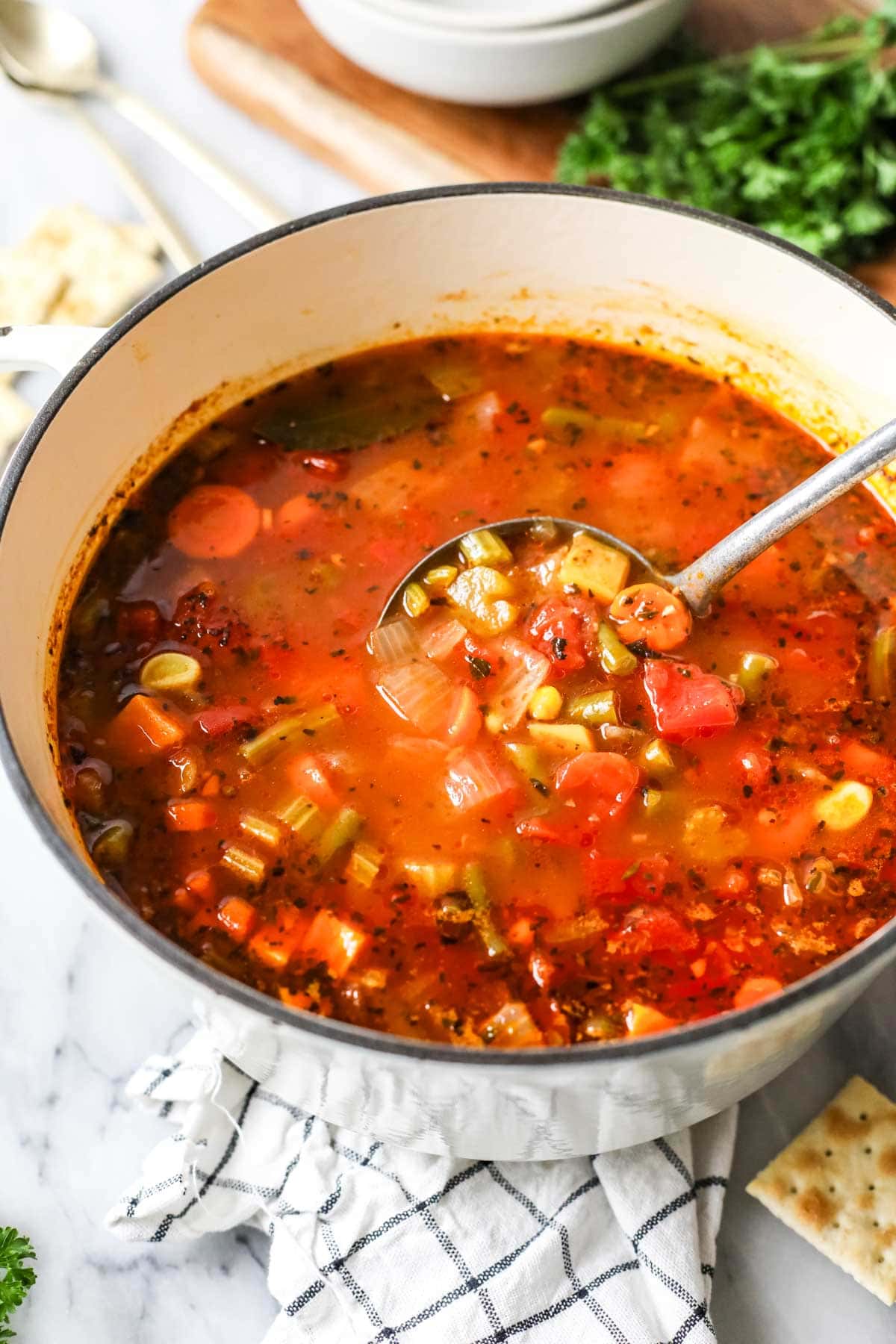 Ladle scooping a serving from a pot of soup made with vegetables.