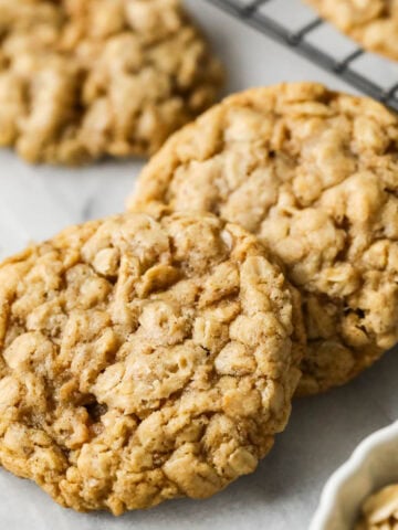 Two sourdough oatmeal cookies beside a cooling rack of more cookies.