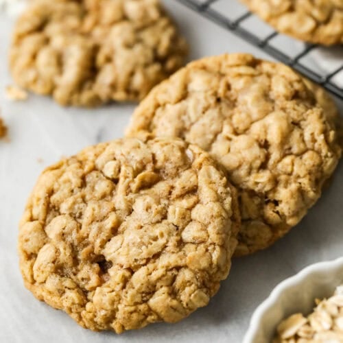 Two sourdough oatmeal cookies beside a cooling rack of more cookies.