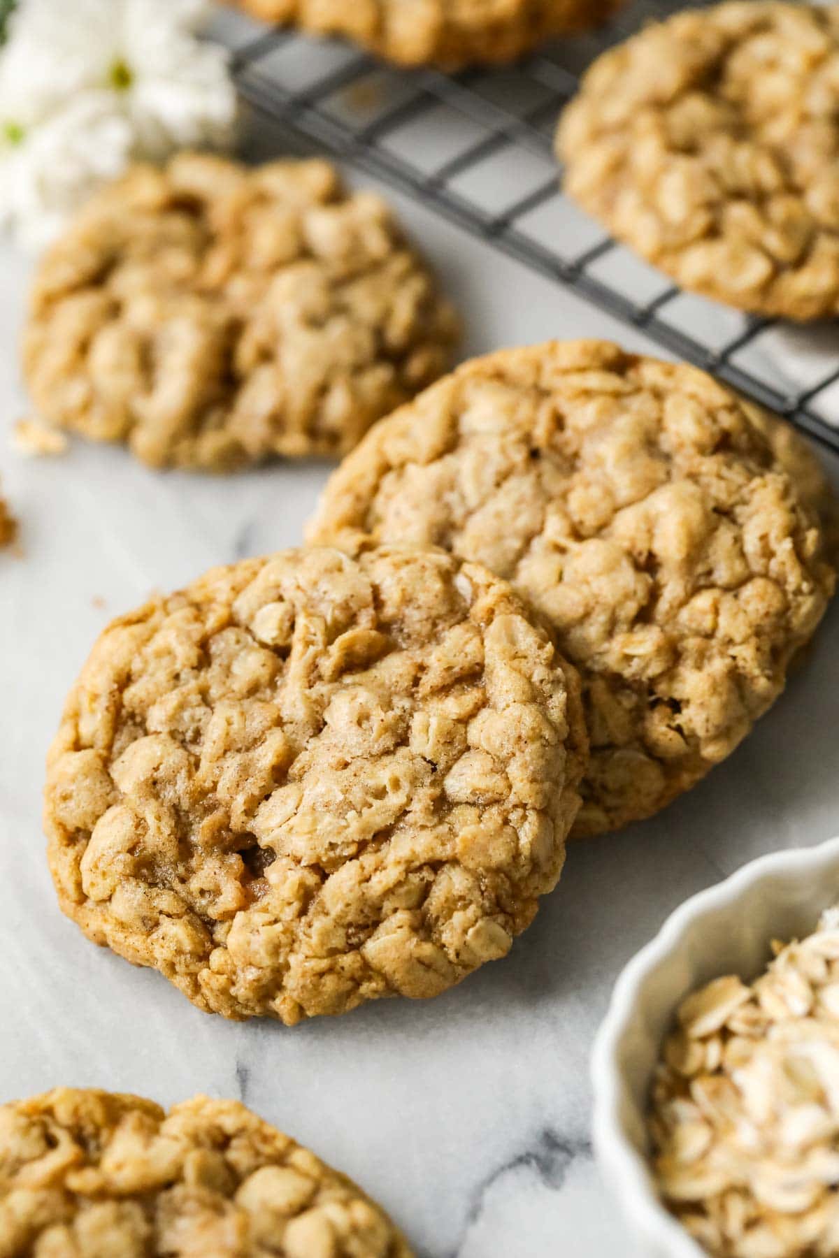 Two sourdough oatmeal cookies beside a cooling rack of more cookies.