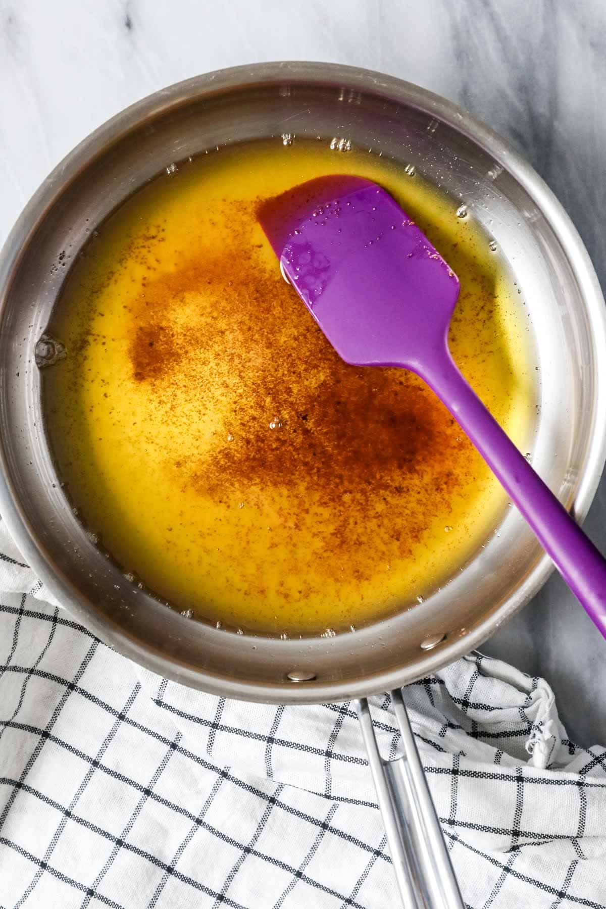 Overhead view of browned butter in a saucepan with a purple spatula.