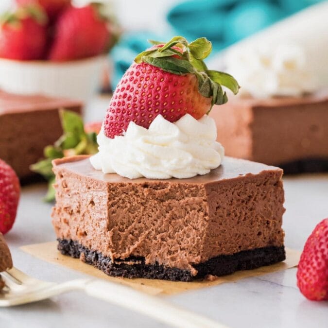 Chocolate cheesecake bar topped with whipped cream and a strawberry.