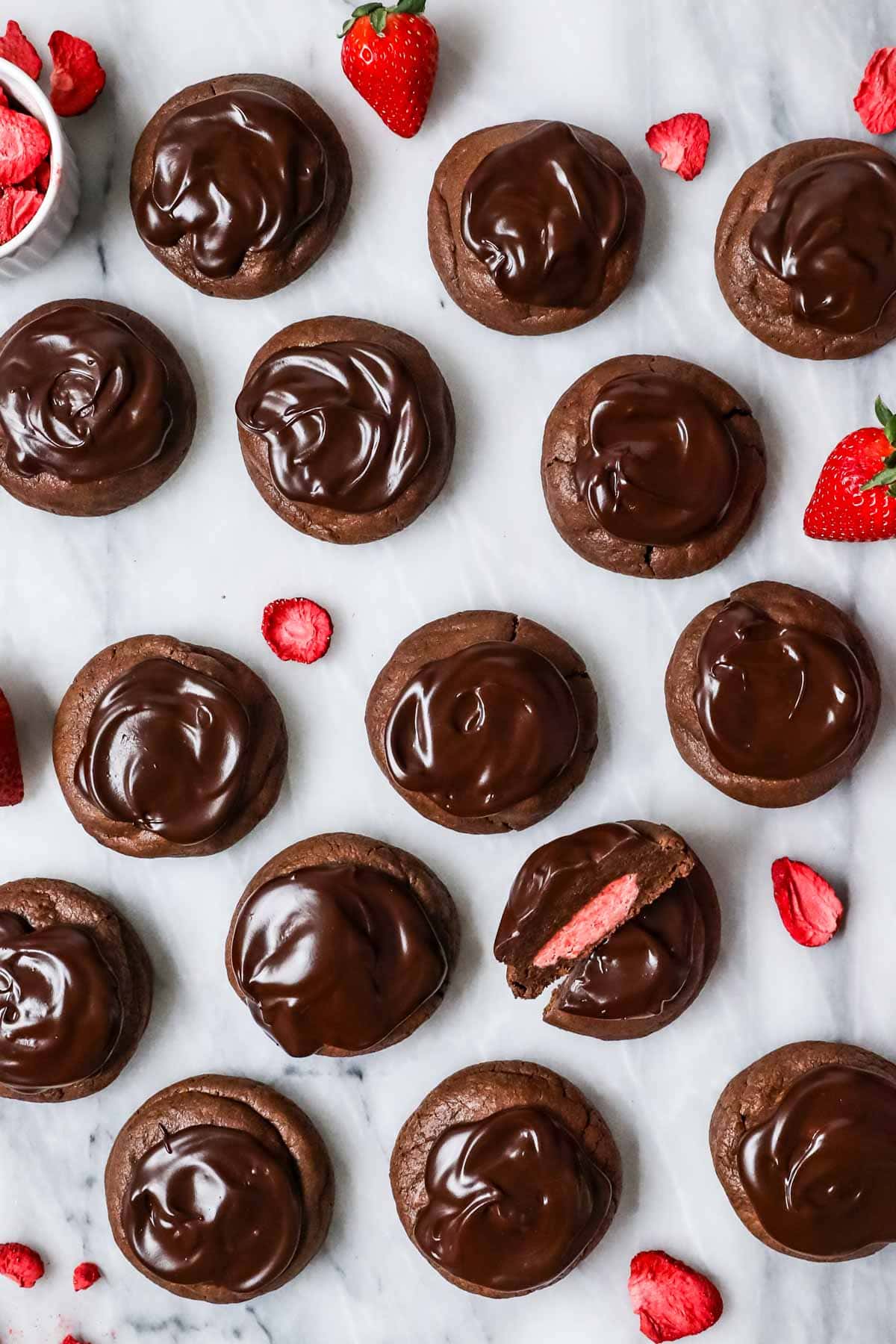 Overhead view of chocolate covered strawberry cookies with one cookie cut in half to show a strawberry frosting center.