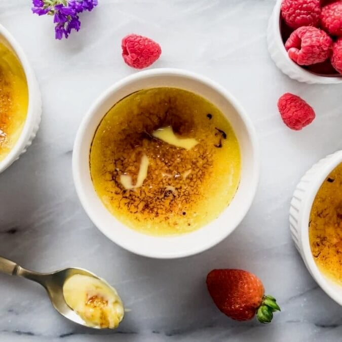 Overhead view of creme brulee surrounded by fresh berries and flowers.
