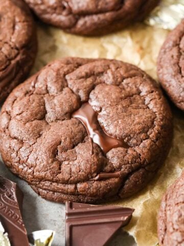 Close-up view of a double chocolate chunk cookie surrounded by more cookies and chocolate chunks.