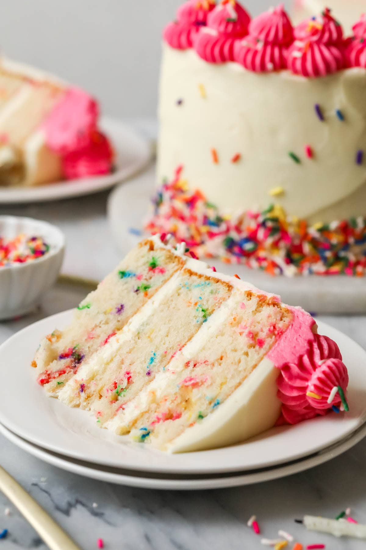 Slice of funfetti cake on a plate with the remaining cake in the background.