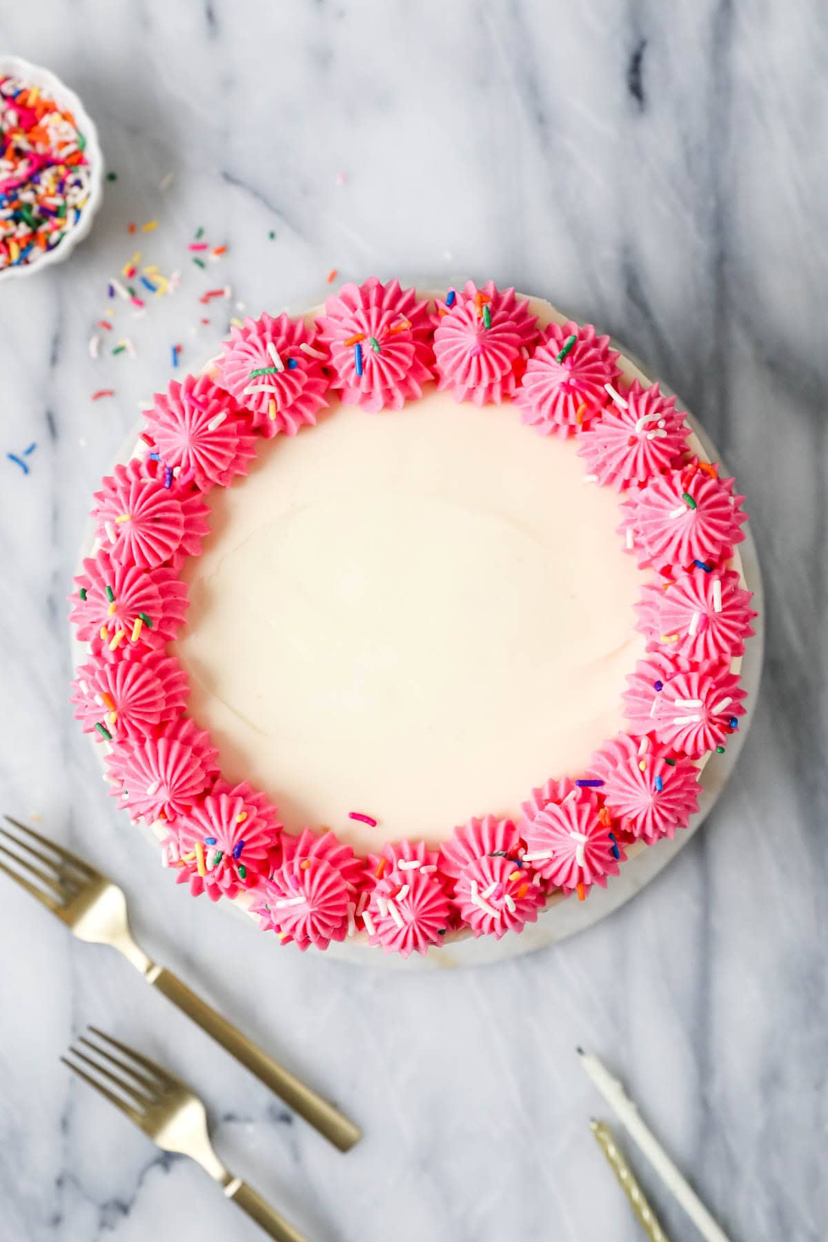 Overhead view of a cake with a piped pink frosting border topped with sprinkles.