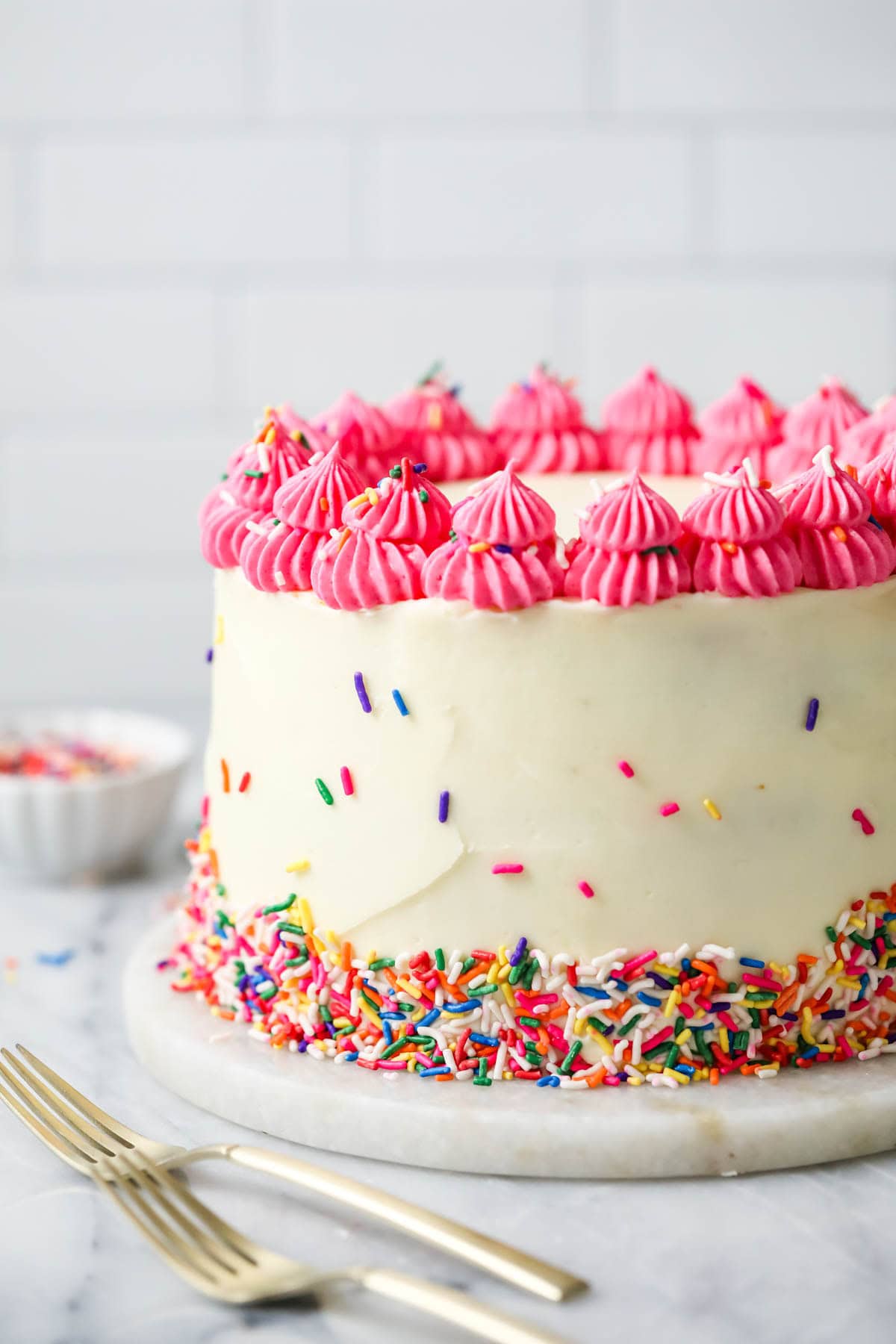 Tall funfetti cake decorated with a bright pink frosting border and sprinkles.