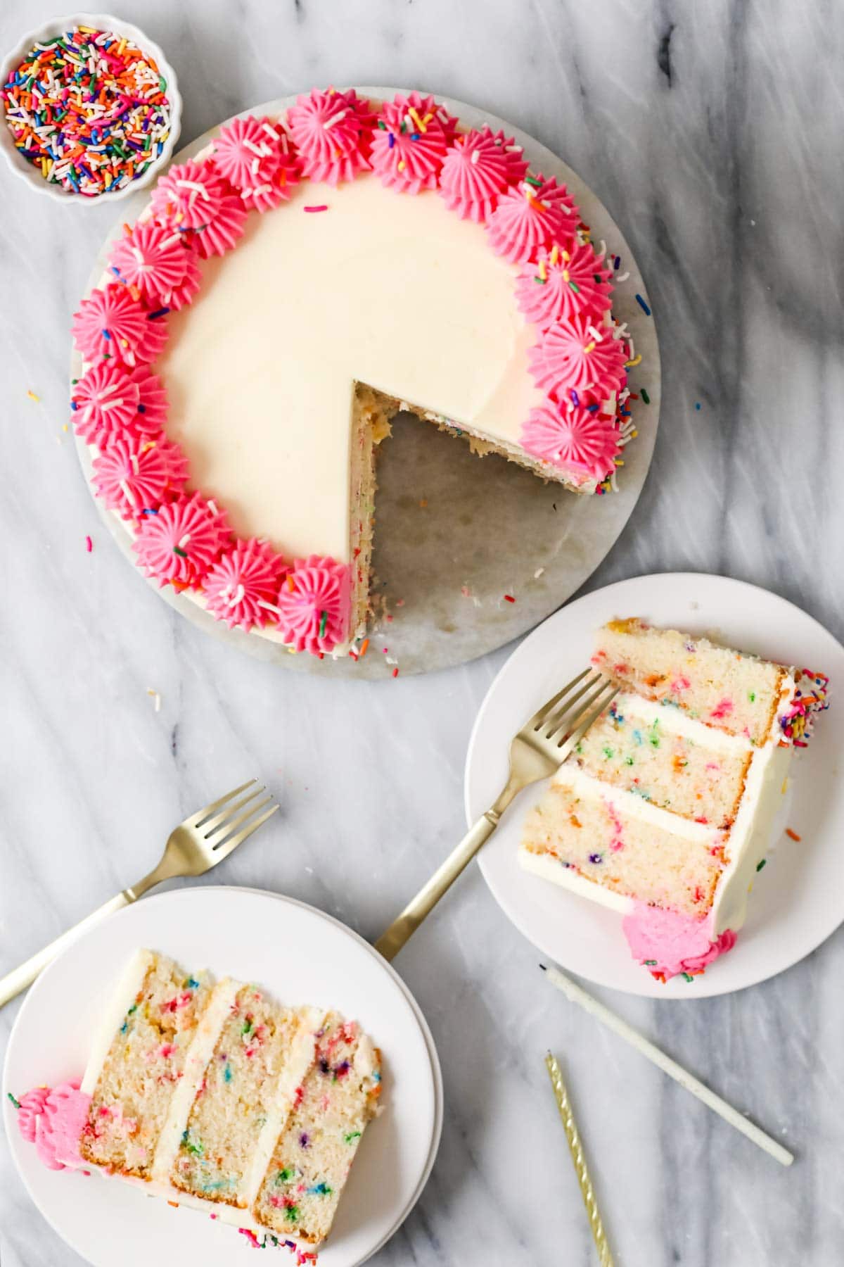 Overhead view of a cake with a piped pink frosting border with two slices cut on plates beside it.