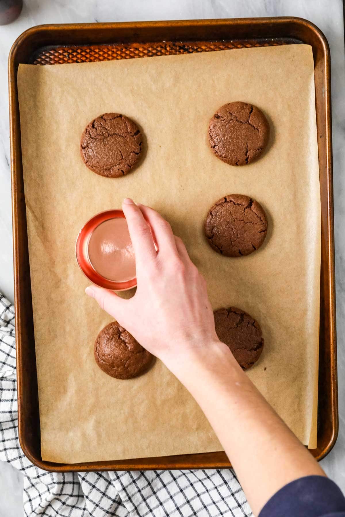 Hands pressing a glass onto chocolate cookies to flatten them after baking.