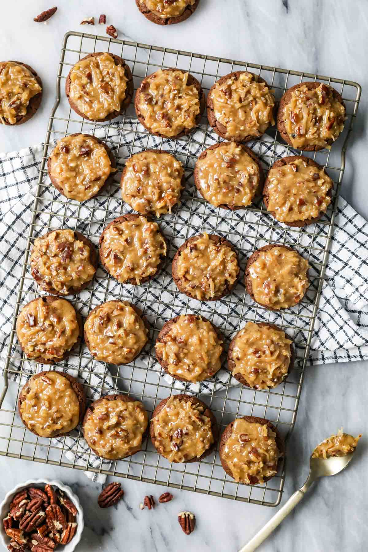 Overhead view of a cooling rack of chocolate cookies topped with a pecan and coconut topping to mimic german chocolate cake.