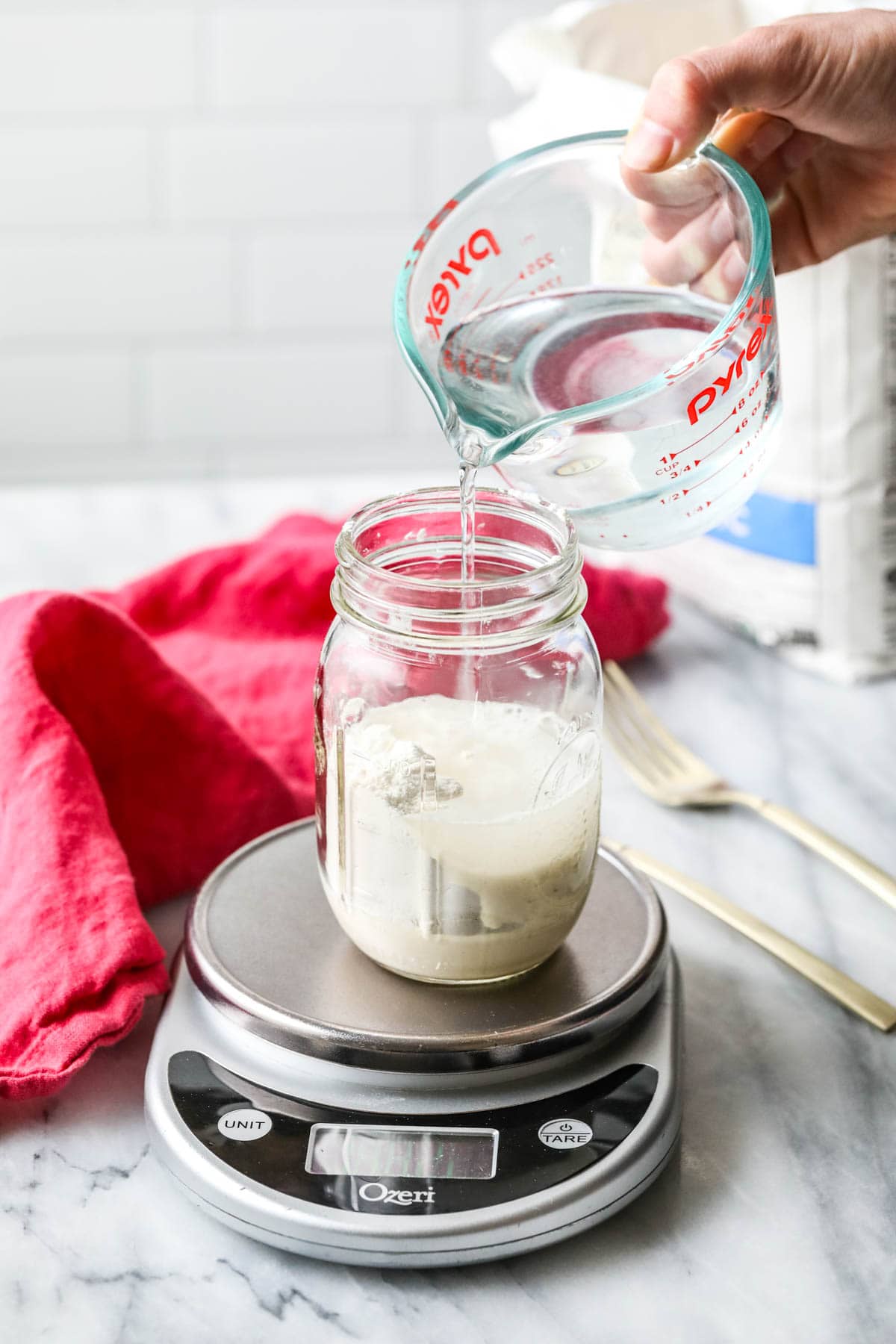 pouring water into sourdough starter