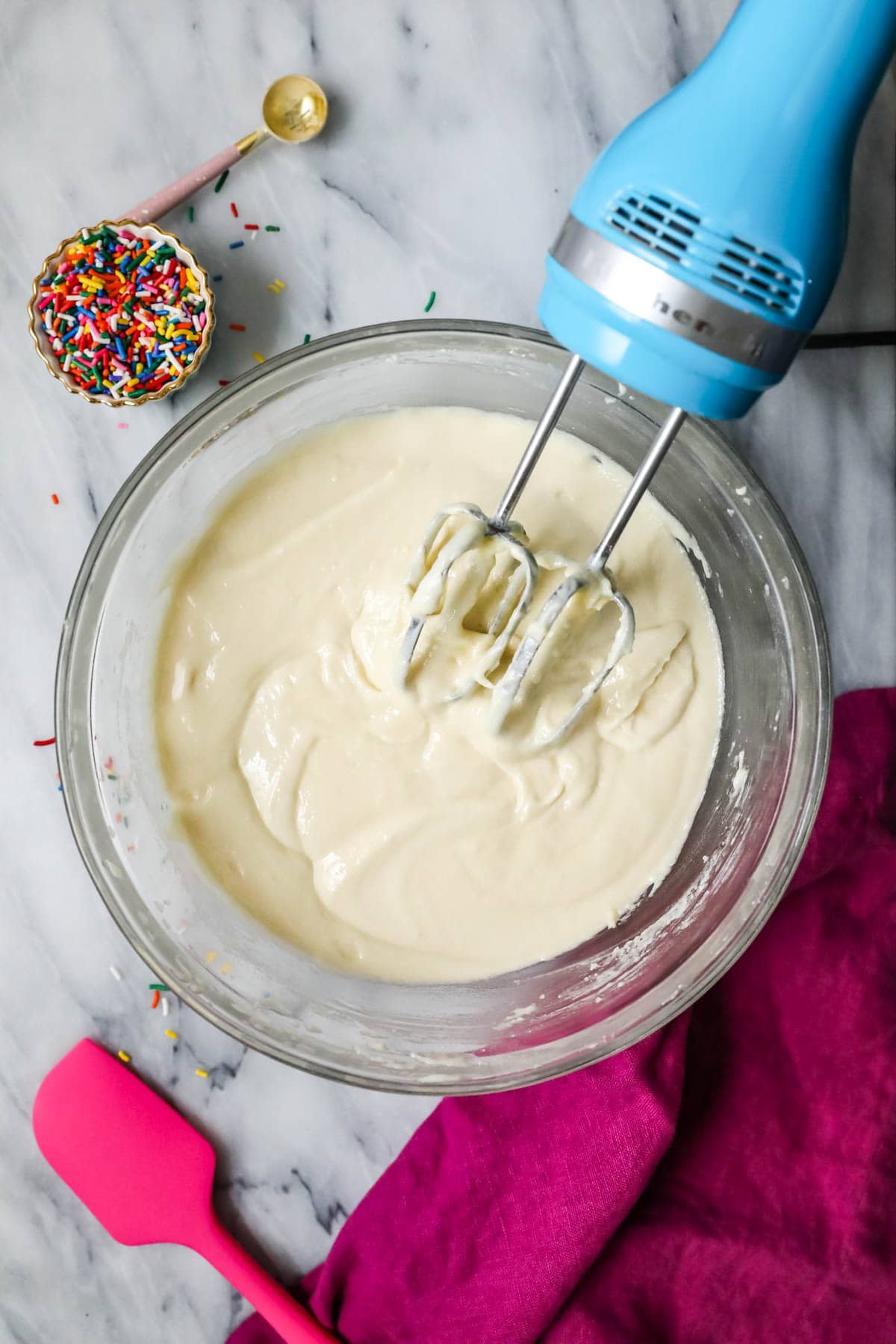 Overhead view of a bowl of cake batter being stirred with an electric mixer.