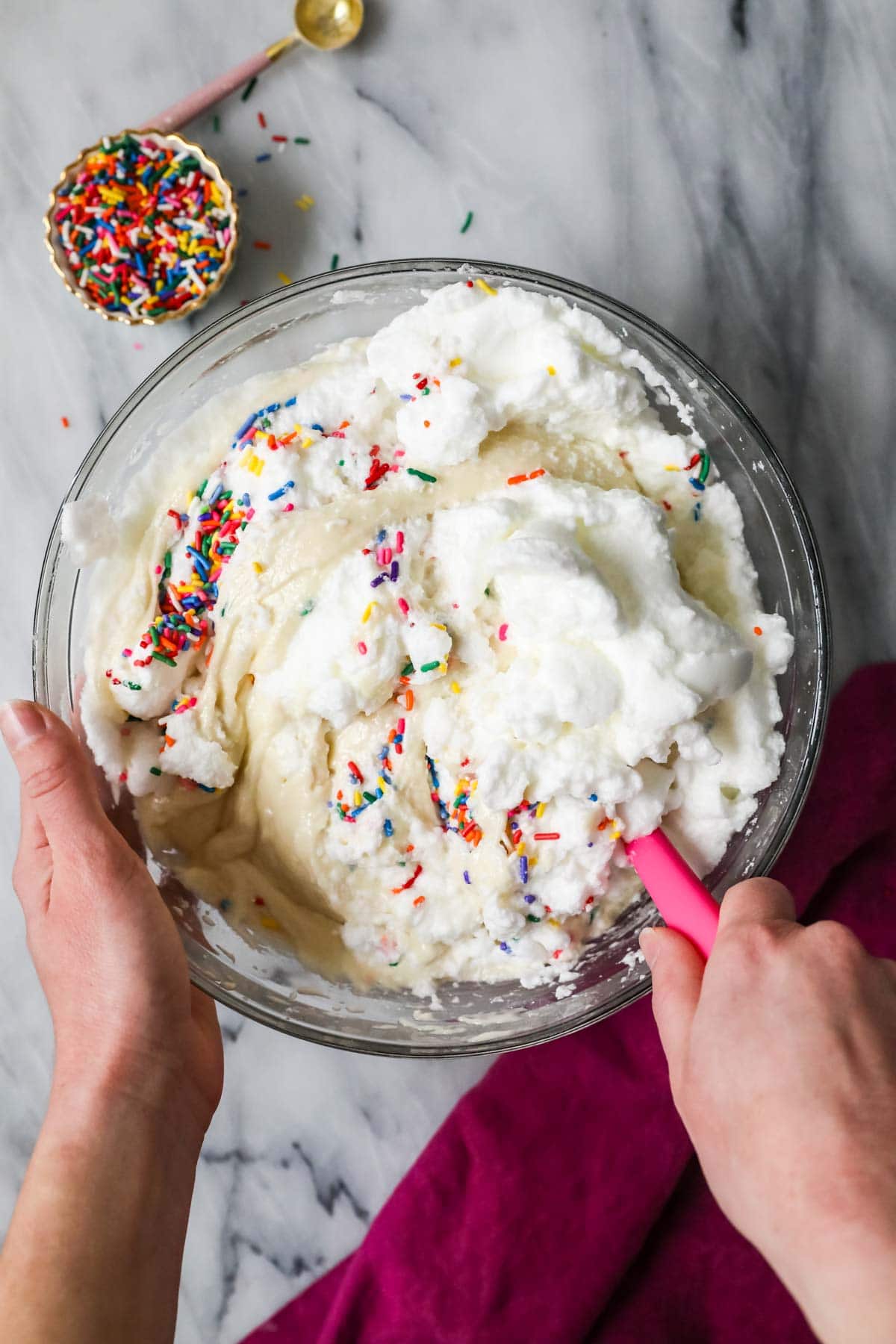 Overhead view of egg whites and sprinkles being folded into cake batter.