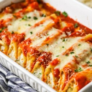 Manicotti in a casserole dish topped with sauce and cheese.