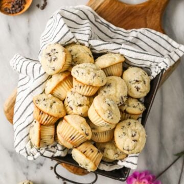 Overhead view of mini muffins in a baking pan lined with a striped tea towel.