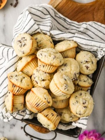 Overhead view of mini muffins in a baking pan lined with a striped tea towel.