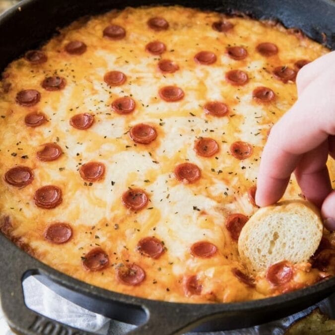Bread being dipped into a pepperoni pizza dip.