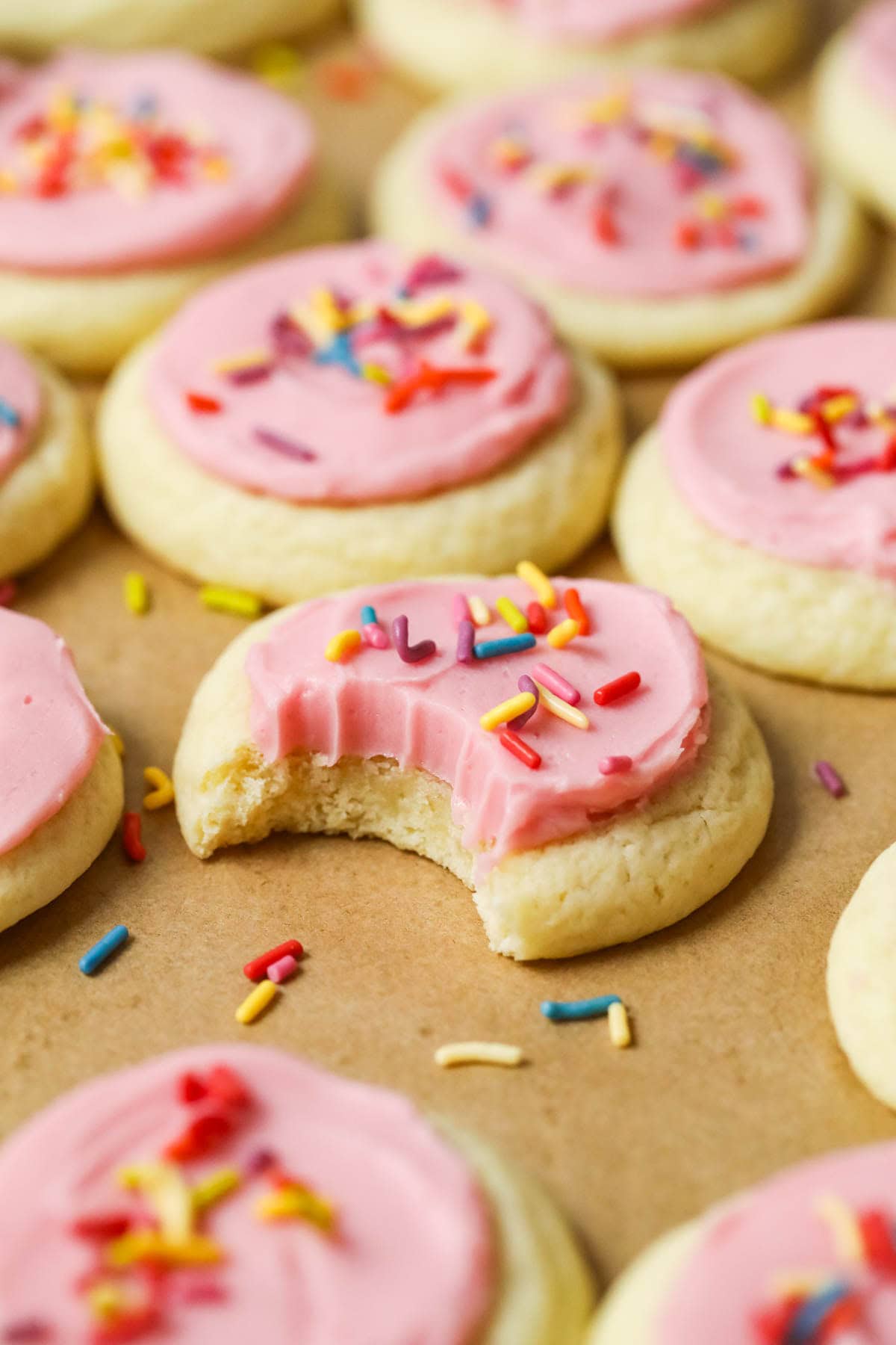 Bite missing from a soft frosted sugar cookie topped with pink icing and sprinkles.