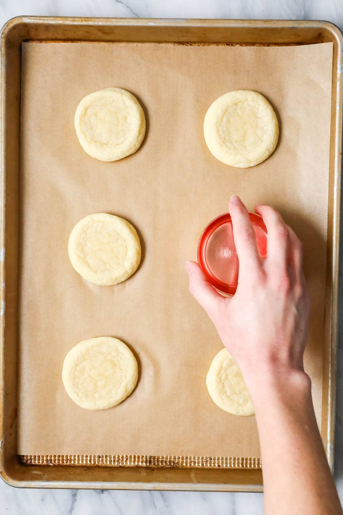 Overhead view of a measuring cup flattening cookies after baking.