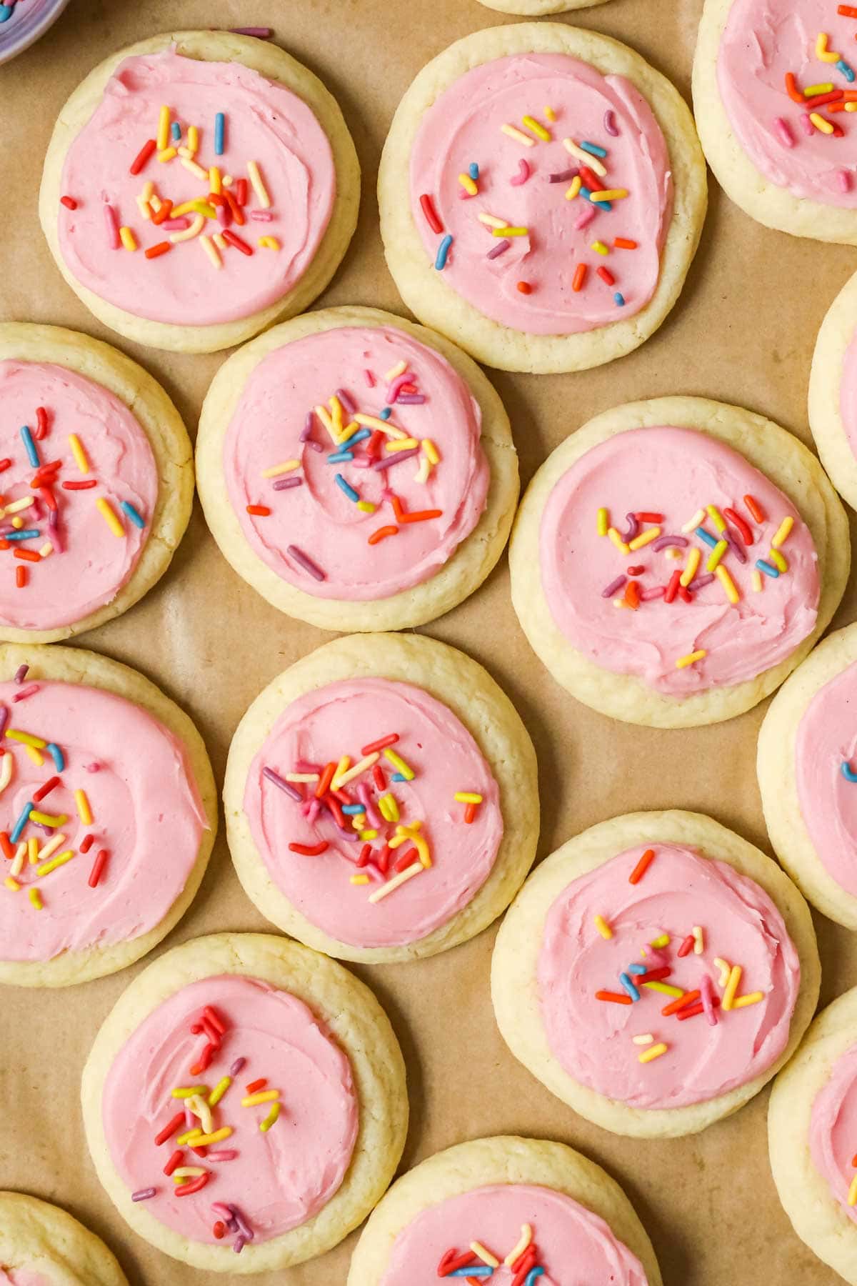 Overhead view of rows of soft sugar cookies topped with pink frosting and sprinkles.