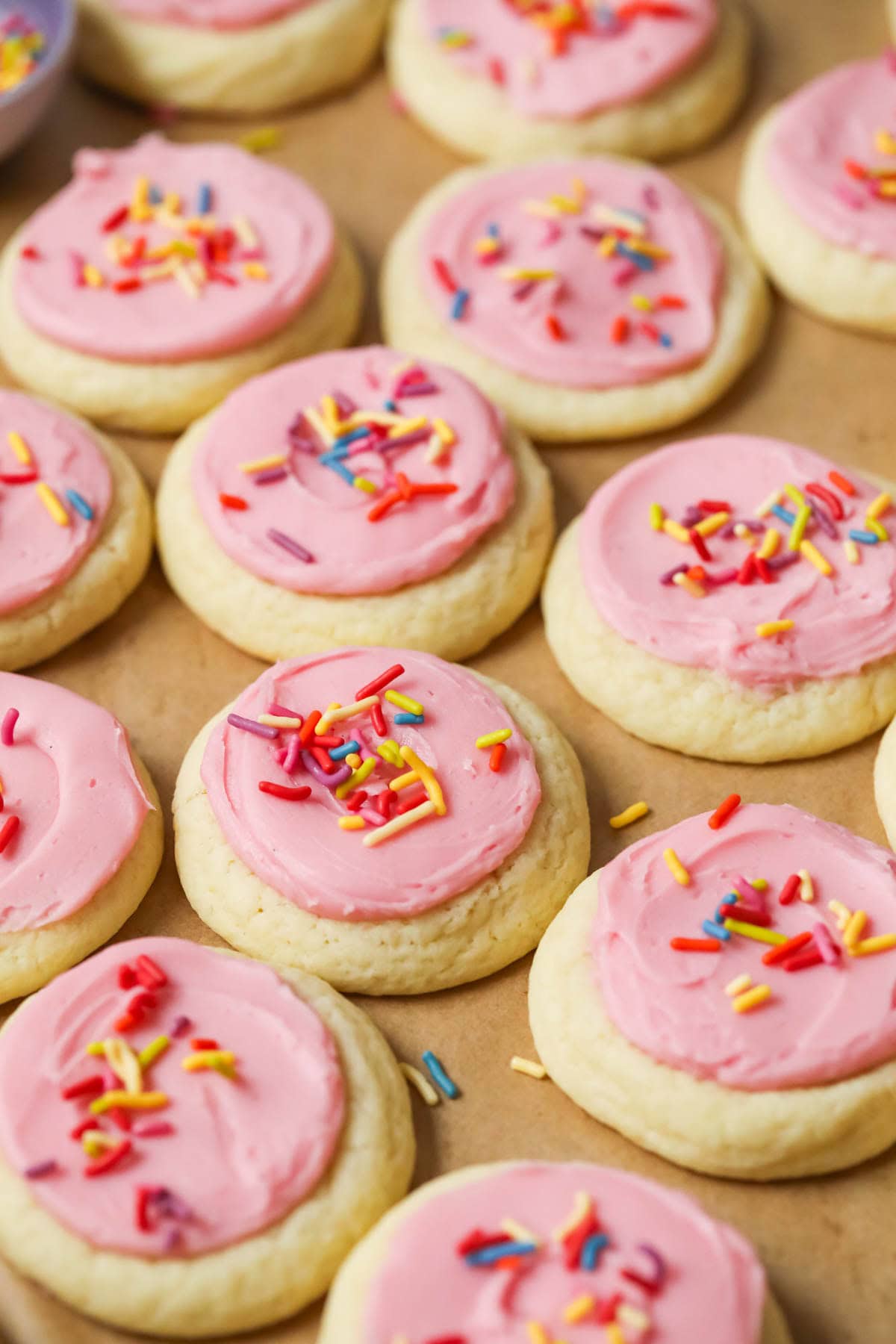 Overhead view of rows of soft frosted sugar cookies topped with pink frosting and sprinkles.