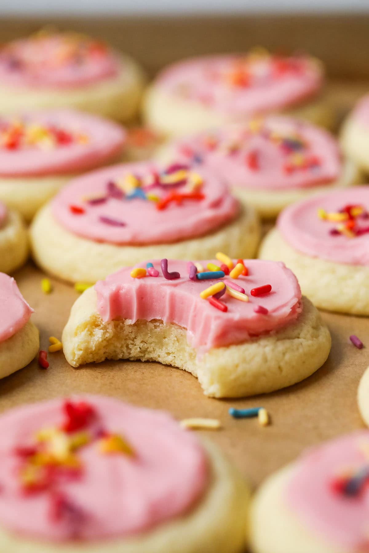 Bite missing from a soft frosted sugar cookie topped with pink icing and sprinkles.