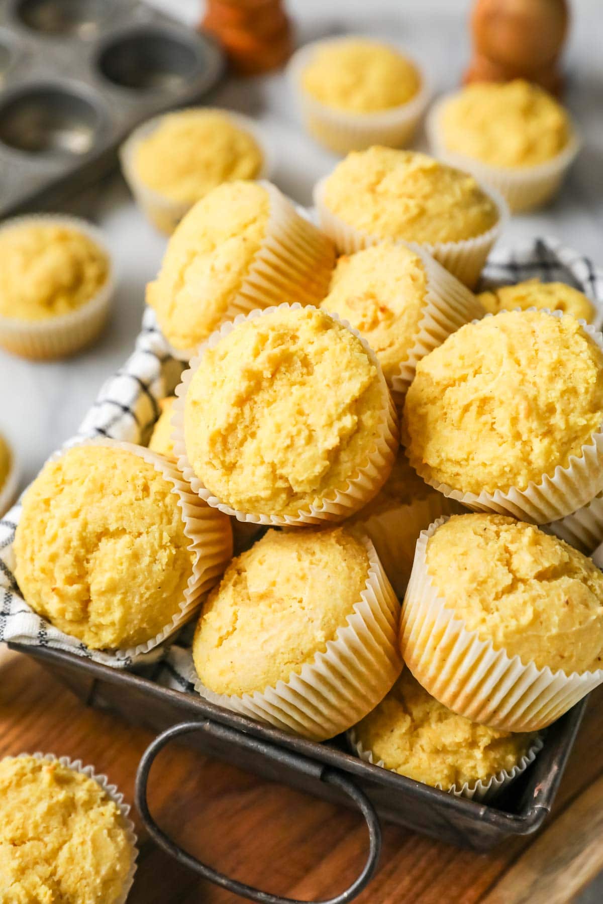 Pile of cornbread muffins in a towel lined metal tray.