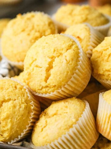 Pile of corn muffins in white muffin wrappers.