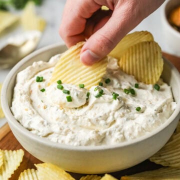 Wavy potato chips being dipped into a homemade sour cream and onion dip.