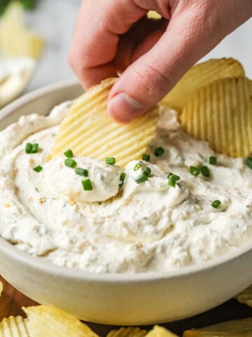 Wavy potato chips being dipped into a homemade sour cream and onion dip.