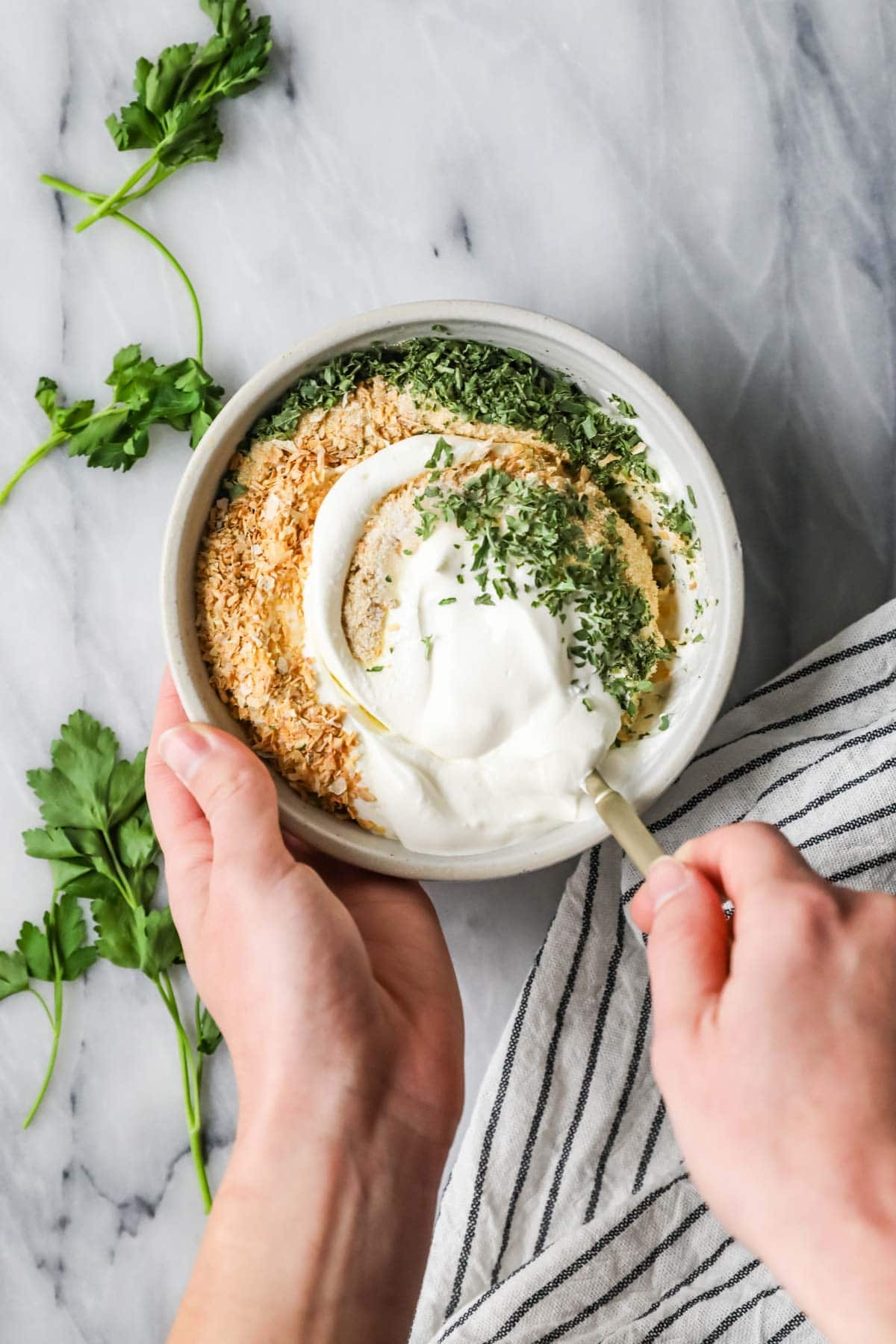 Overhead view of a bowl of sour cream being combined with spices and fresh herbs to make a dip.