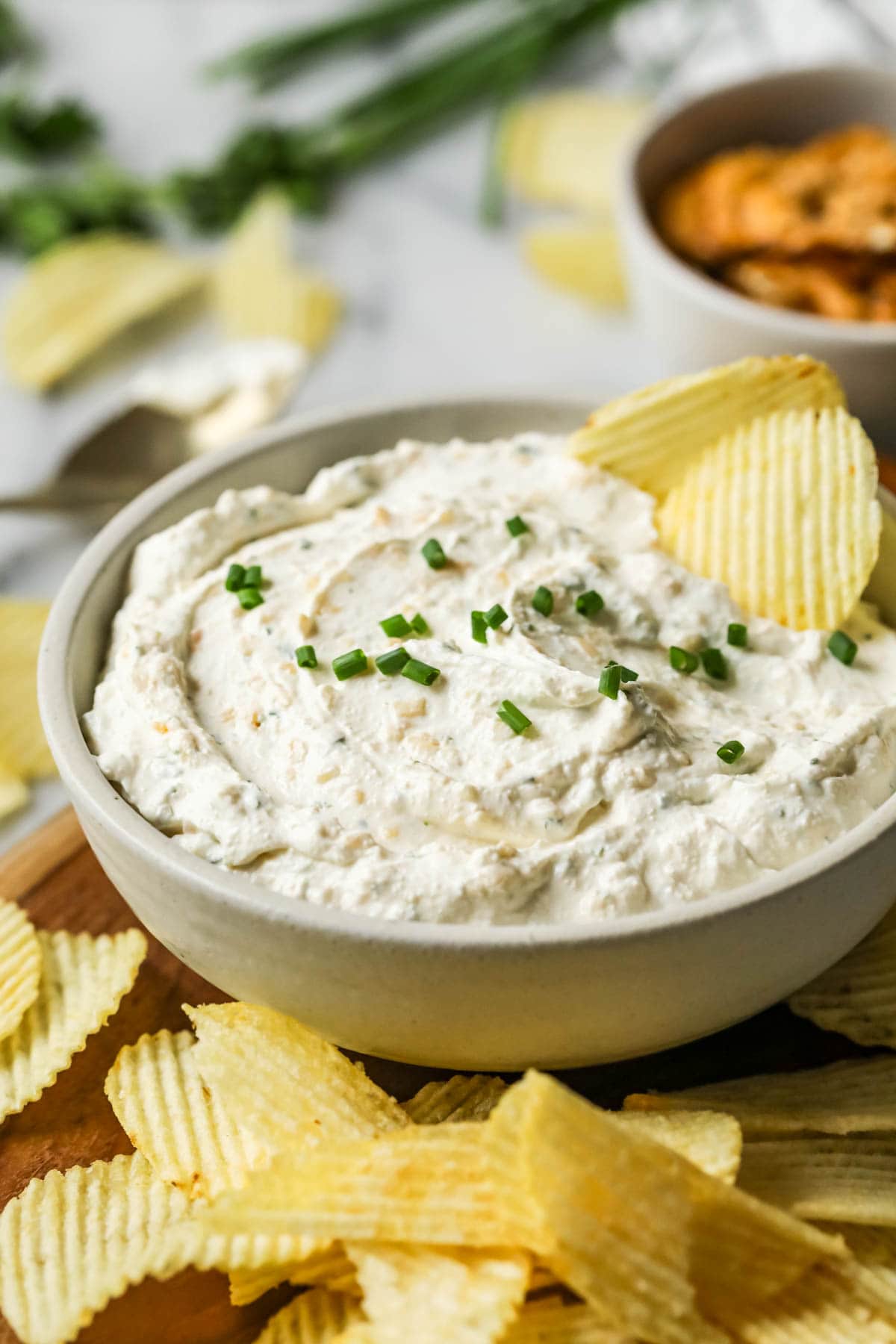 Bowl of homemade sour cream and onion dip garnished with fresh chives and two wavy chips.