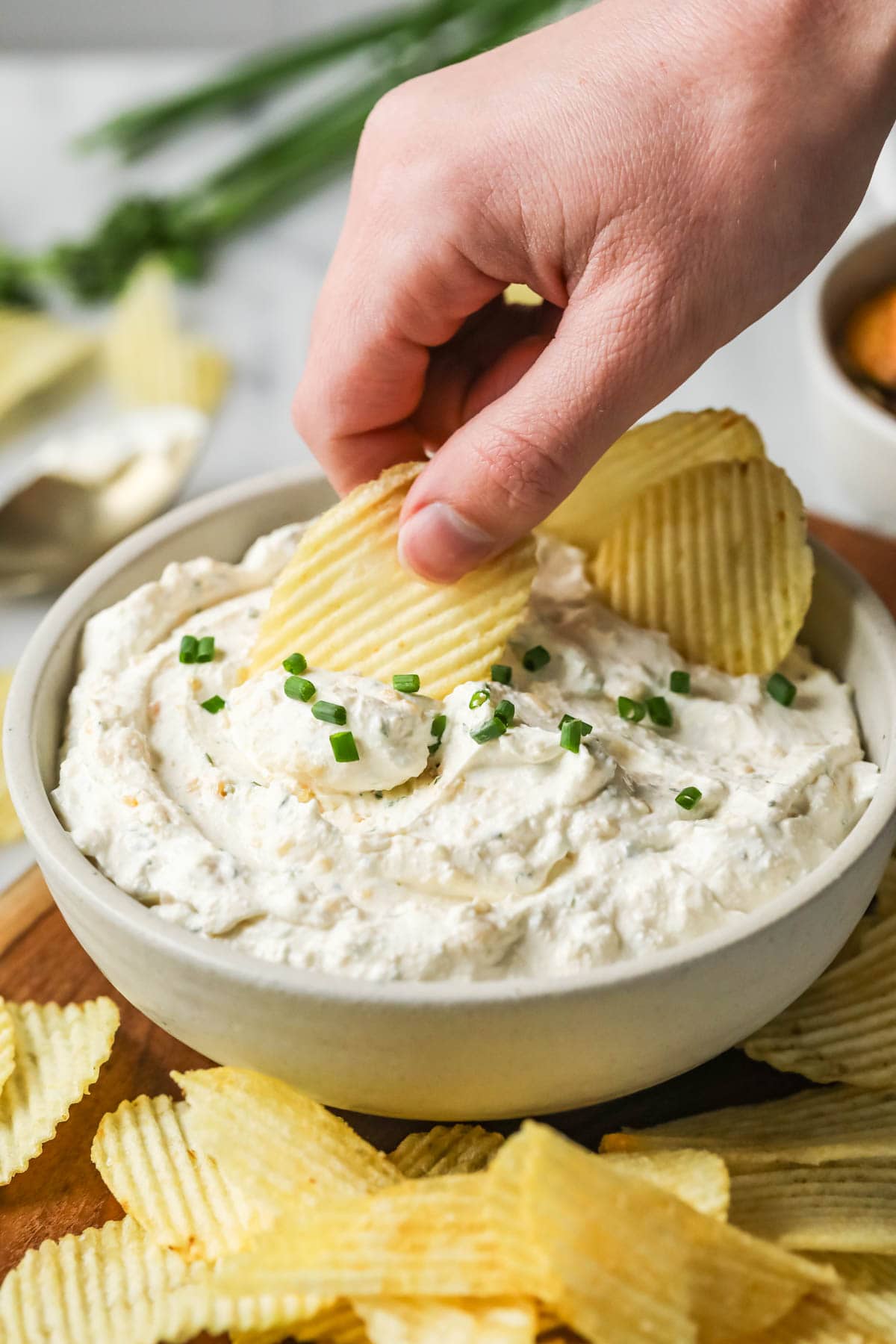 Wavy potato chips being dipped into a homemade sour cream and onion dip.