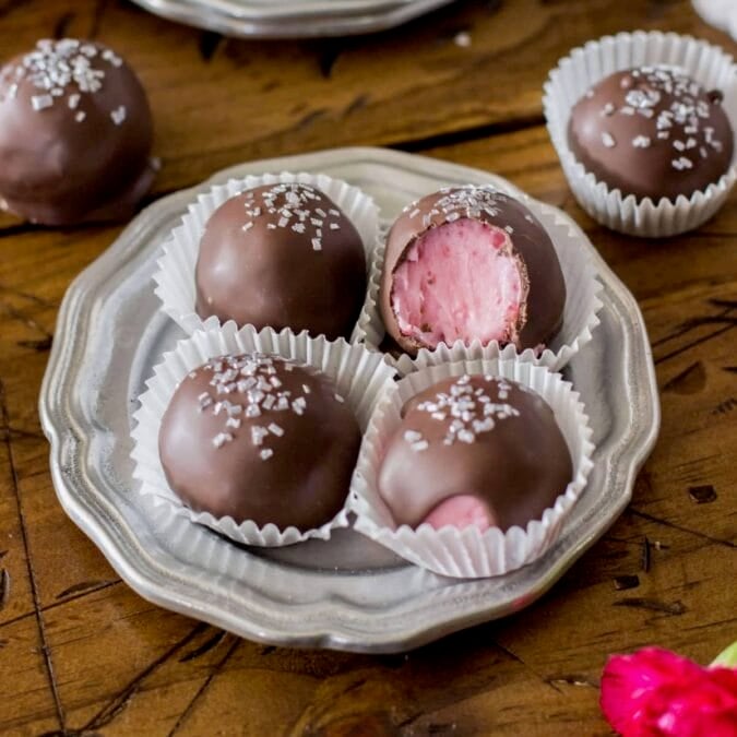 Four strawberry buttercream candies on a small silver plate.