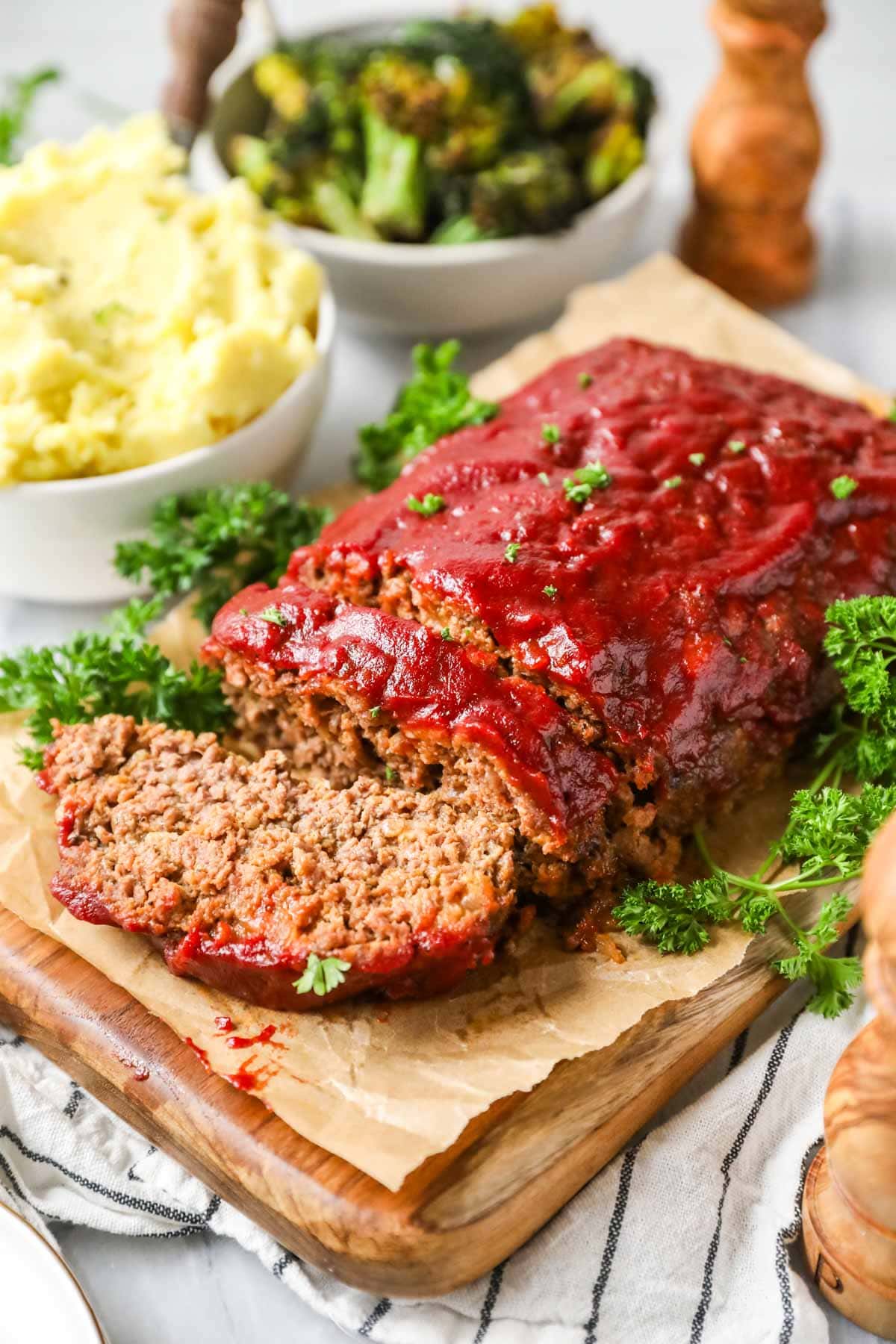 Meatloaf with one slice cut with roasted broccoli and mashed potatoes in the background.