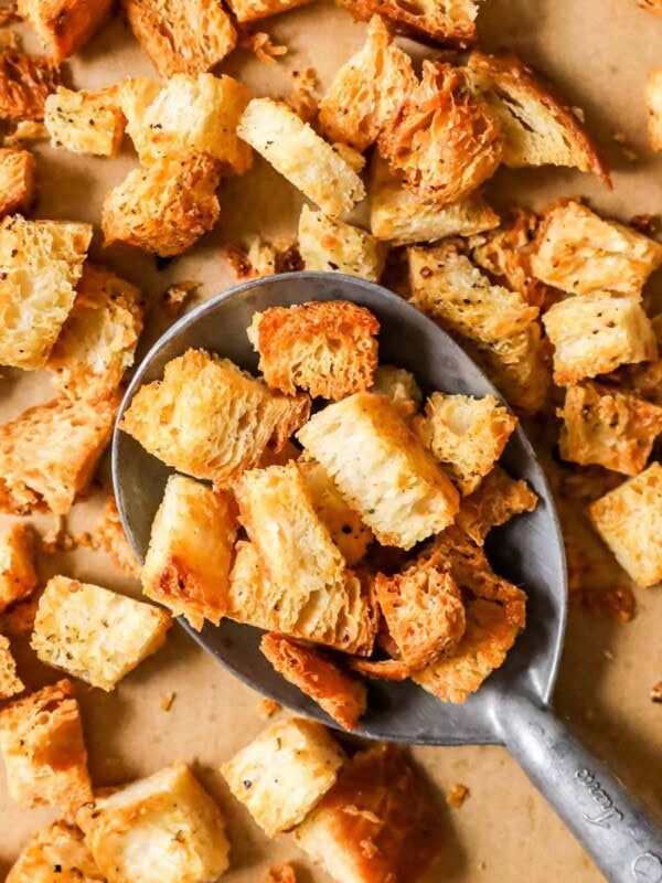 Overhead view of golden brown homemade croutons being scooped off a a baking sheet.