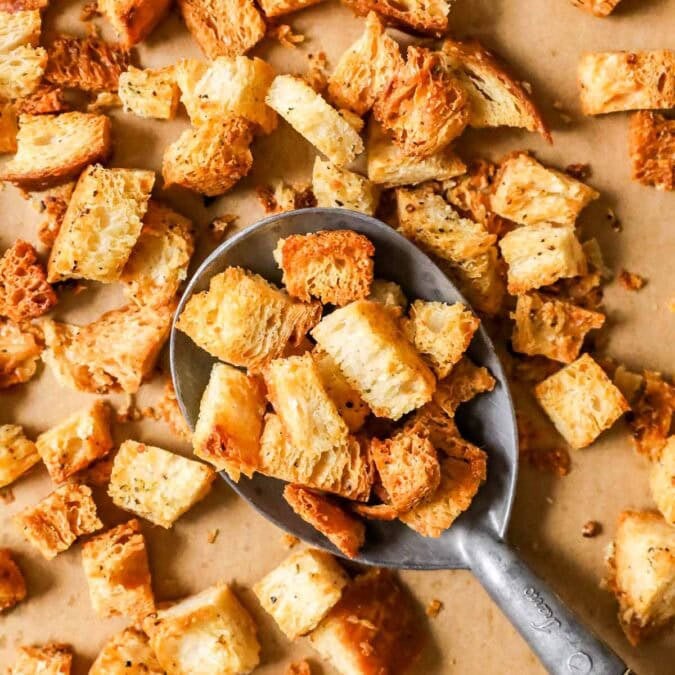 Overhead view of golden brown homemade croutons being scooped off a a baking sheet.