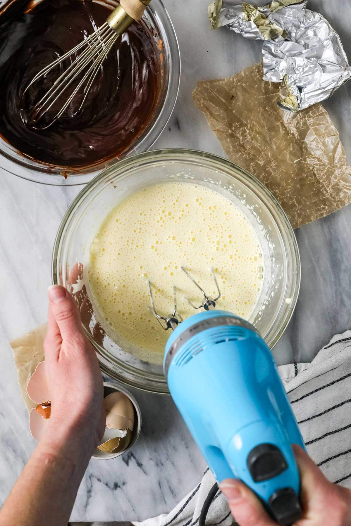 Overhead view of a hand mixer whipping eggs until foamy and light for the shiniest, crinkliest brownie tops.