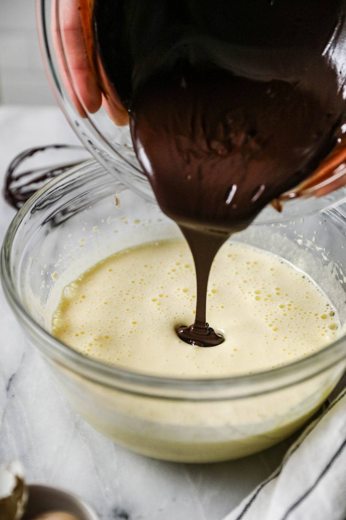 Melted chocolate being poured into a whipped egg mixture.