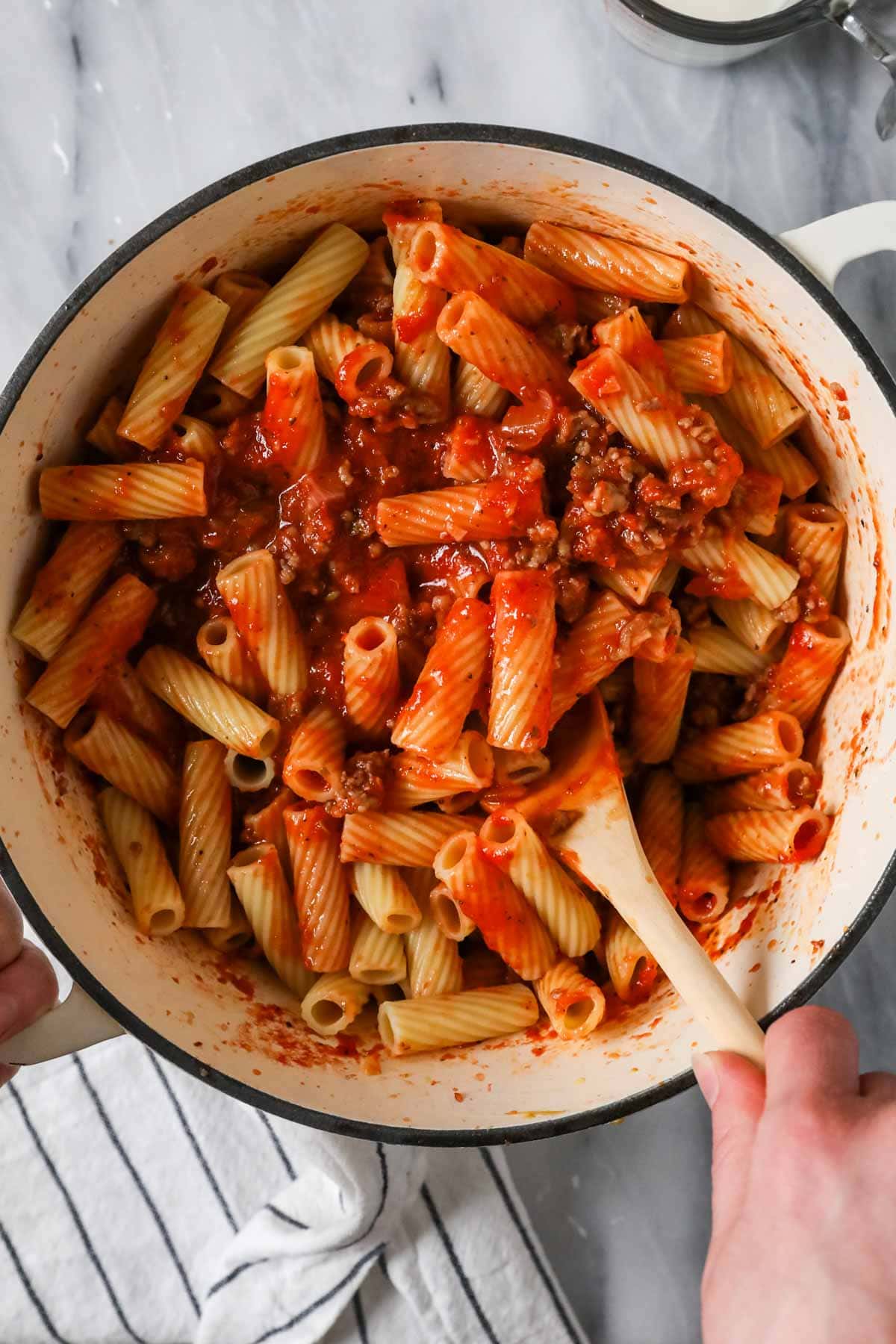 Rigatoni noodles being tossed in a tomato and sausage sauce.
