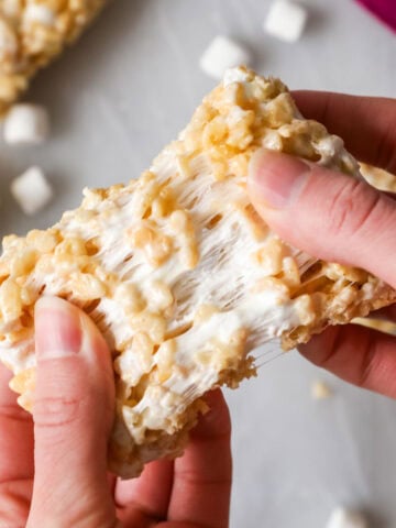 Hands pulling a rice krispie treat apart to show a gooey marshmallow center.