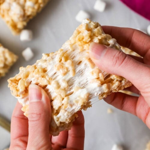 Hands pulling a rice krispie treat apart to show a gooey marshmallow center.