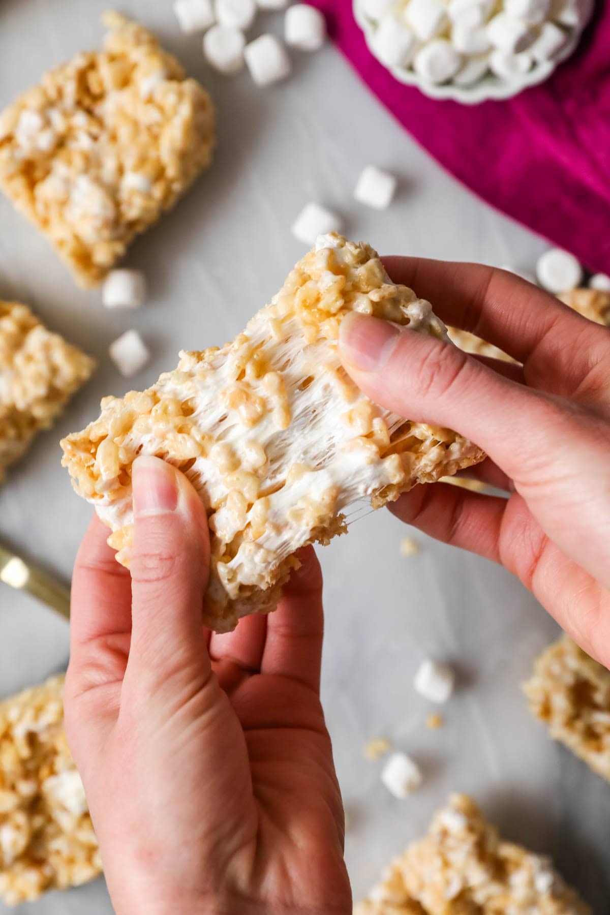 Hands pulling a rice krispie treat apart to show a gooey marshmallow center.