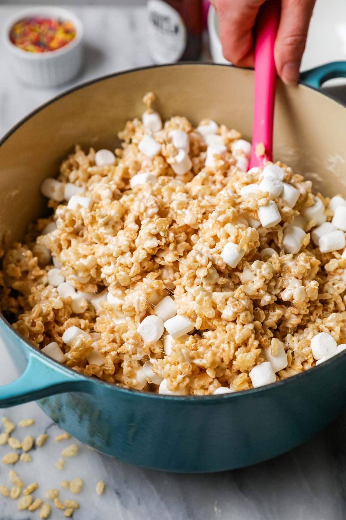 Pink spatula stirring marshmallows into rice krispies cereal.