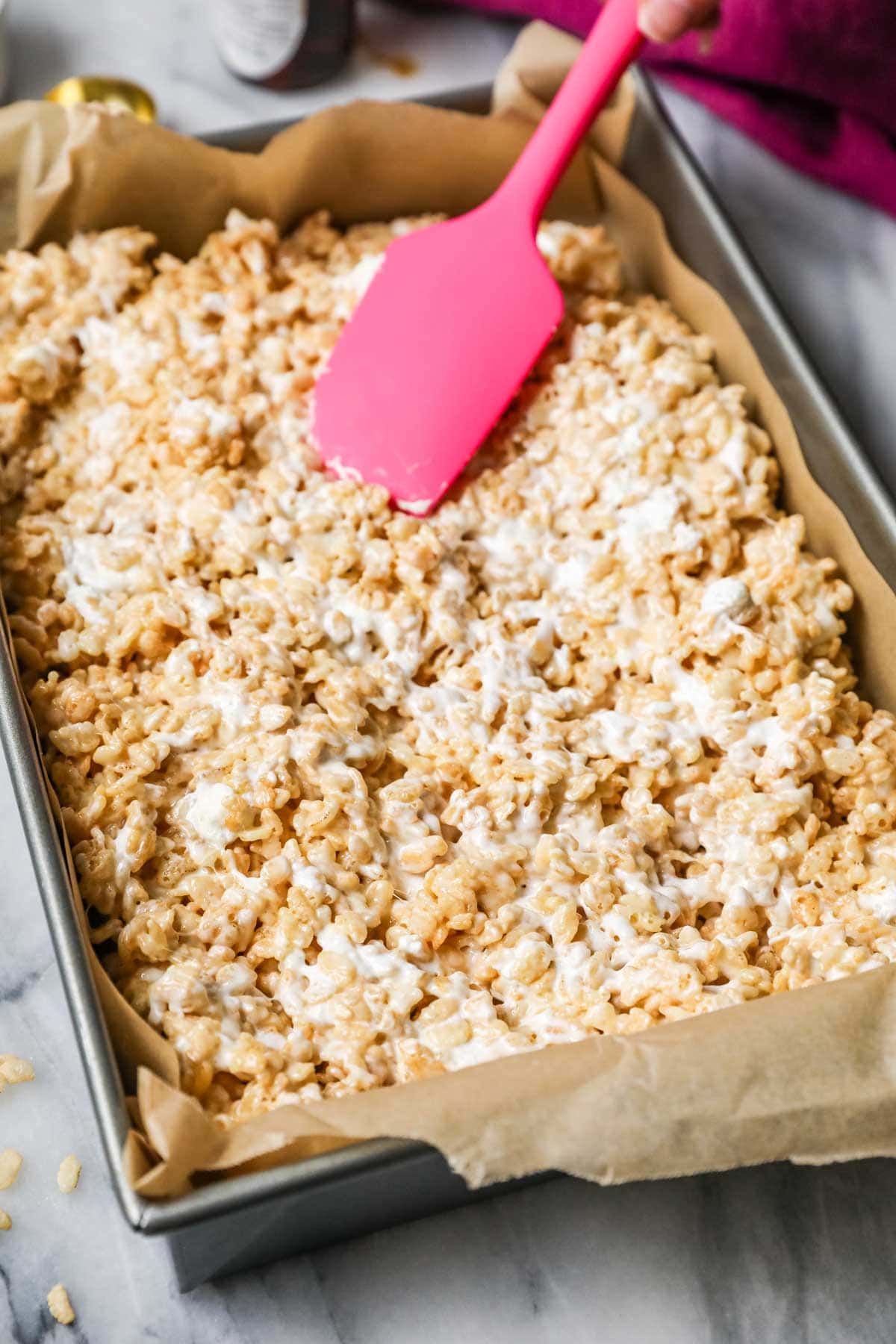 Pink spatula smoothing rice krispie treat mixture into a pan.