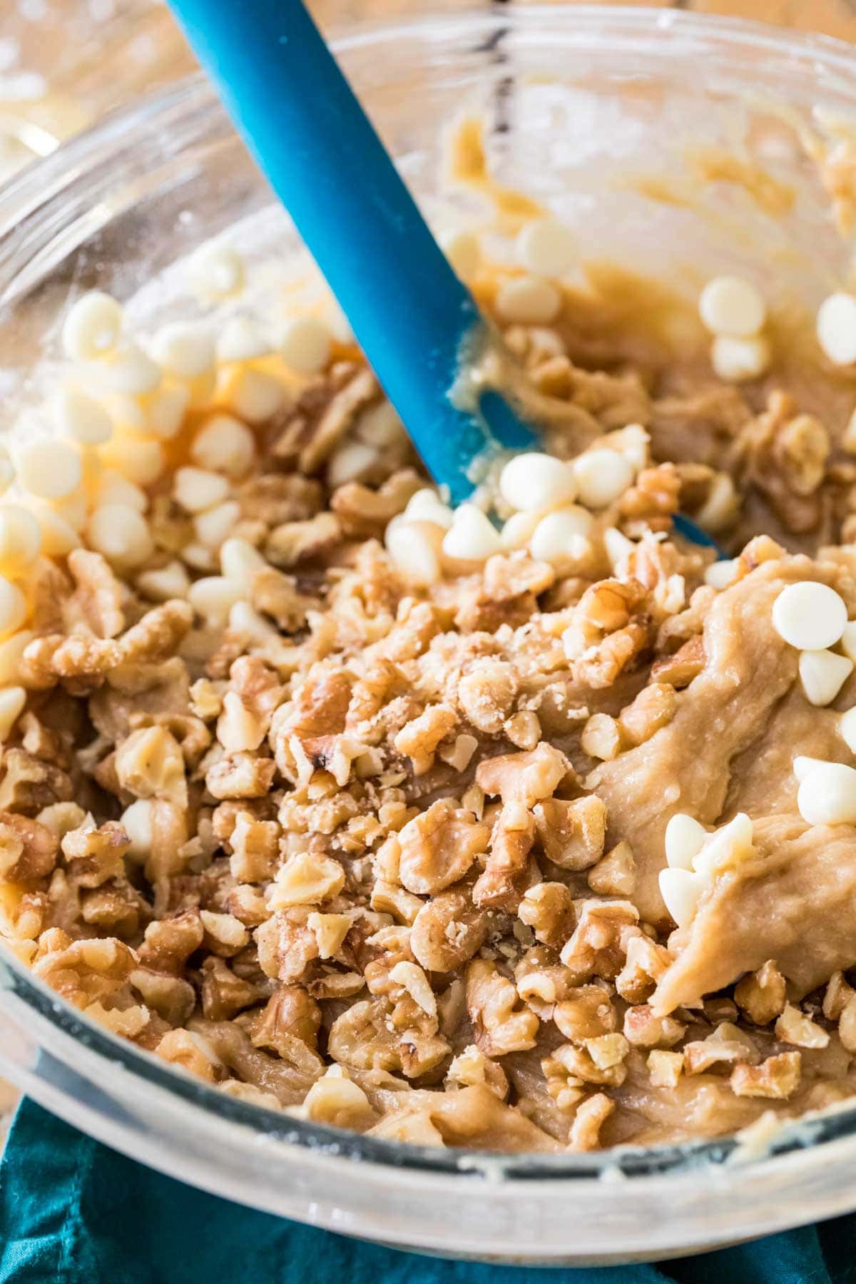 Blondie batter in a bowl with a blue spatula, walnuts and white chocolate have been added but not stirred in yet