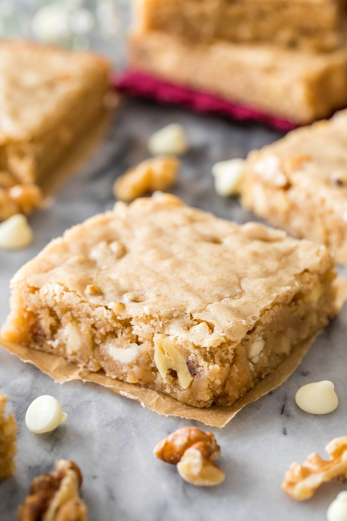 How to make the best chewy BLONDIE recipe! These are so easy and so good, save this recipe! #blondies #barcookie Cut square of blondie on marble, surrounded by more blondies and nuts and white chocolate