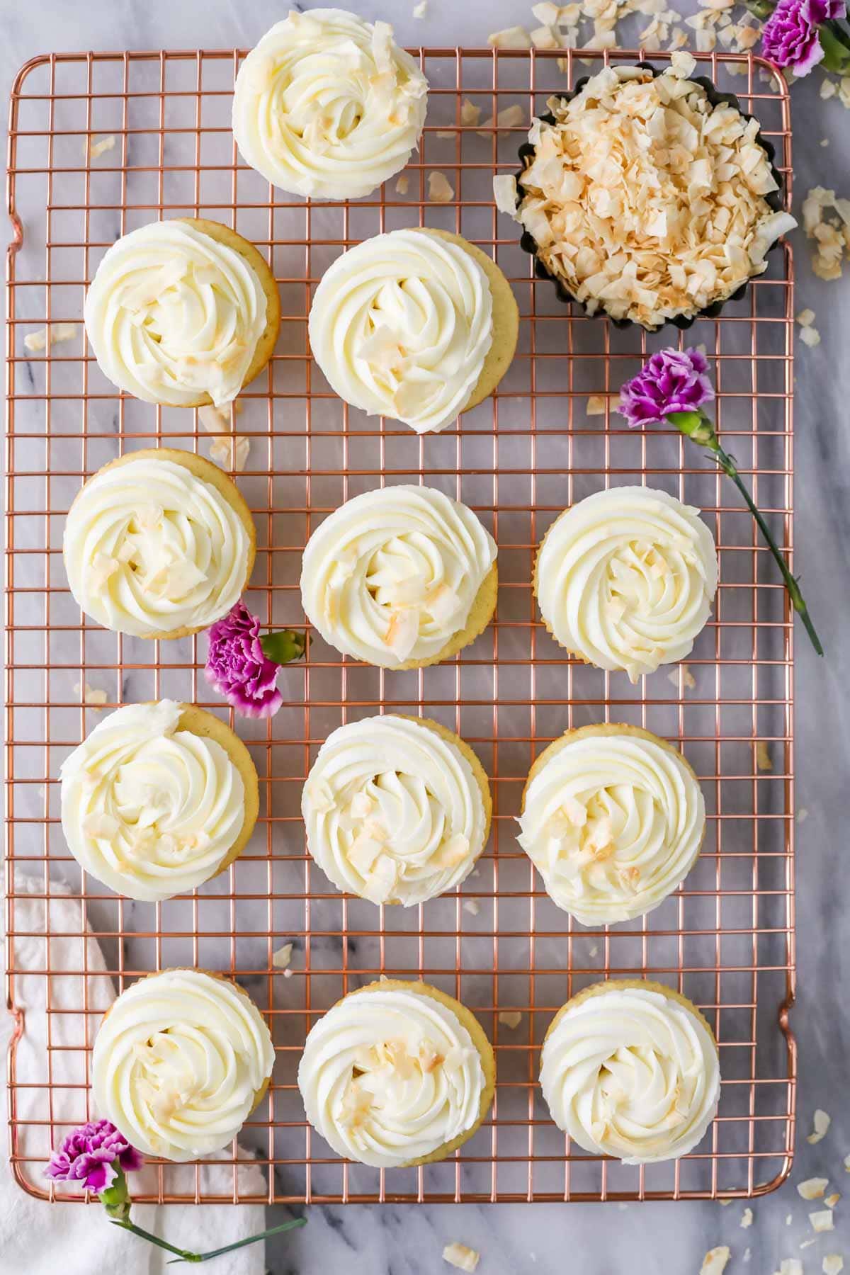Overhead view of cupcakes topped with swirls of cream cheese frosting and toasted coconut flakes.