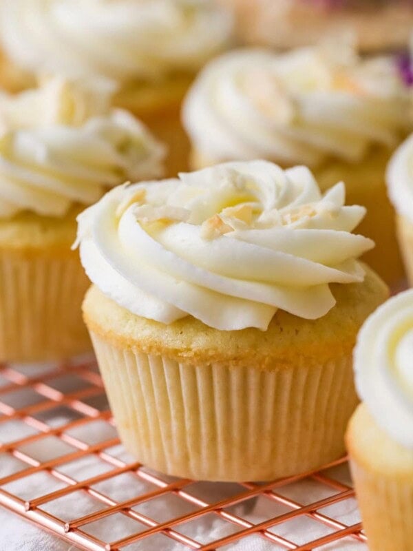 Rows of coconut cupcakes on a cooling rack with purple flowers in the background.